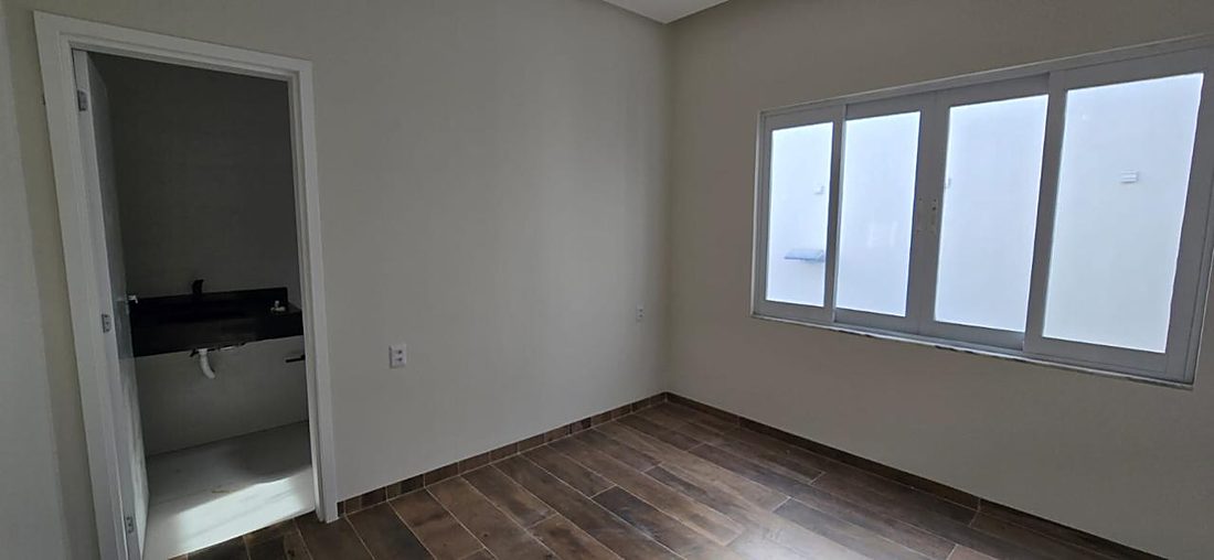 Suíte com piso amadeirado e banheiro privativo ao fundo